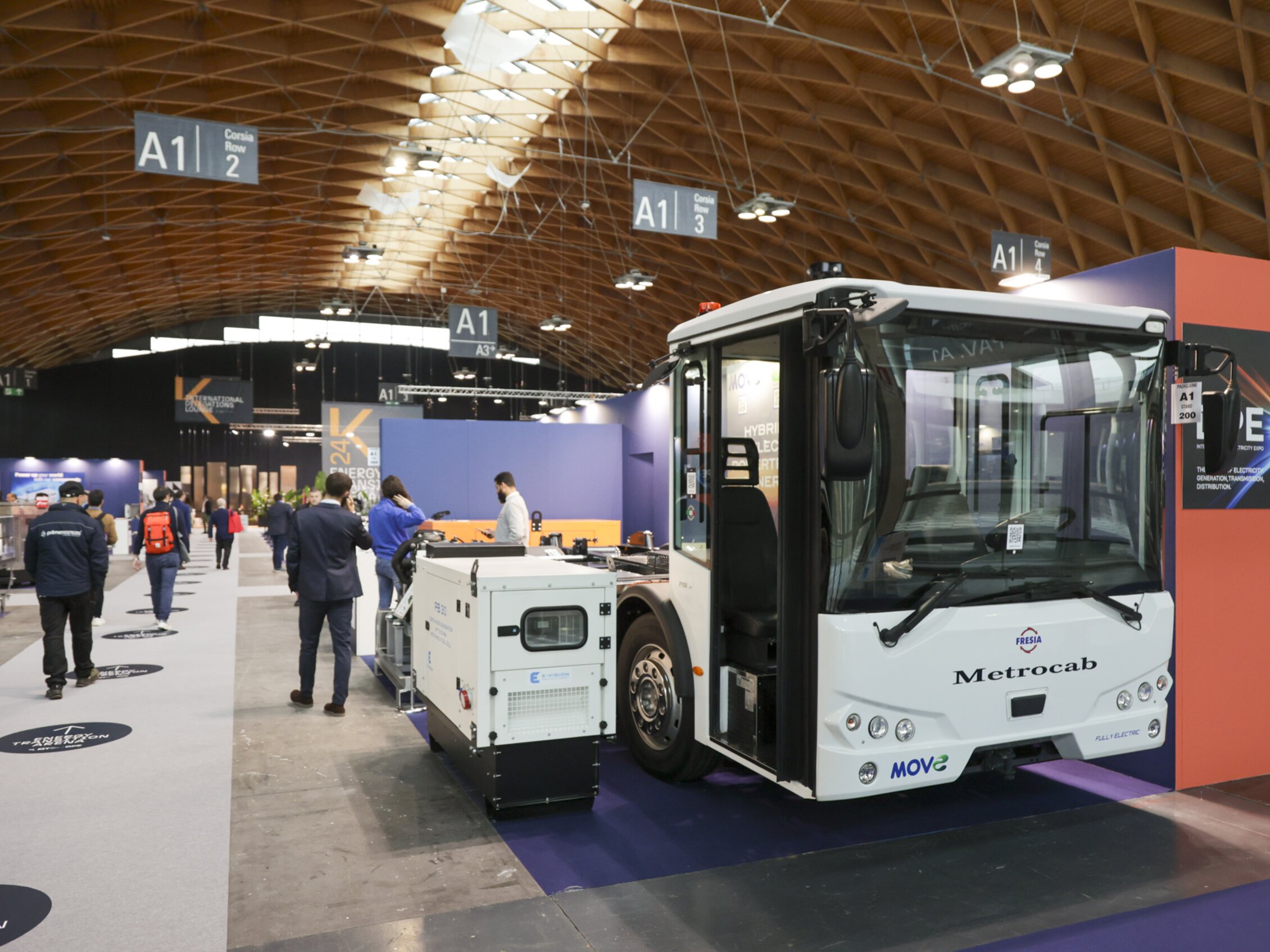 Veicolo elettrico MetroCub esposto all'interno di uno stand durante DPE circondato da persone che camminano tra gli stand