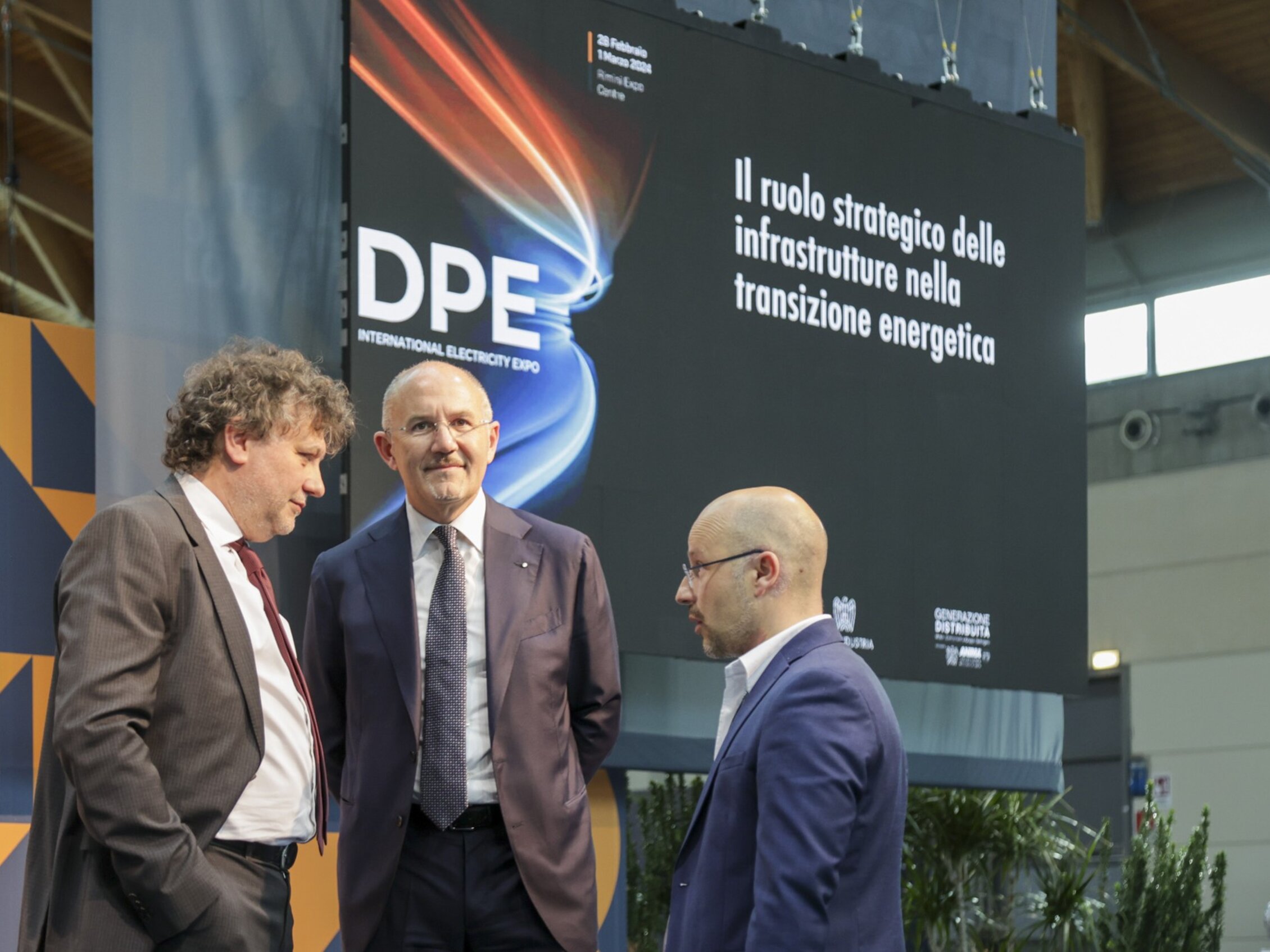 tre uomini parlano fra di loro sul palco di una conferenza sul ruolo strategico delle infrastrutture nella transizione energetica