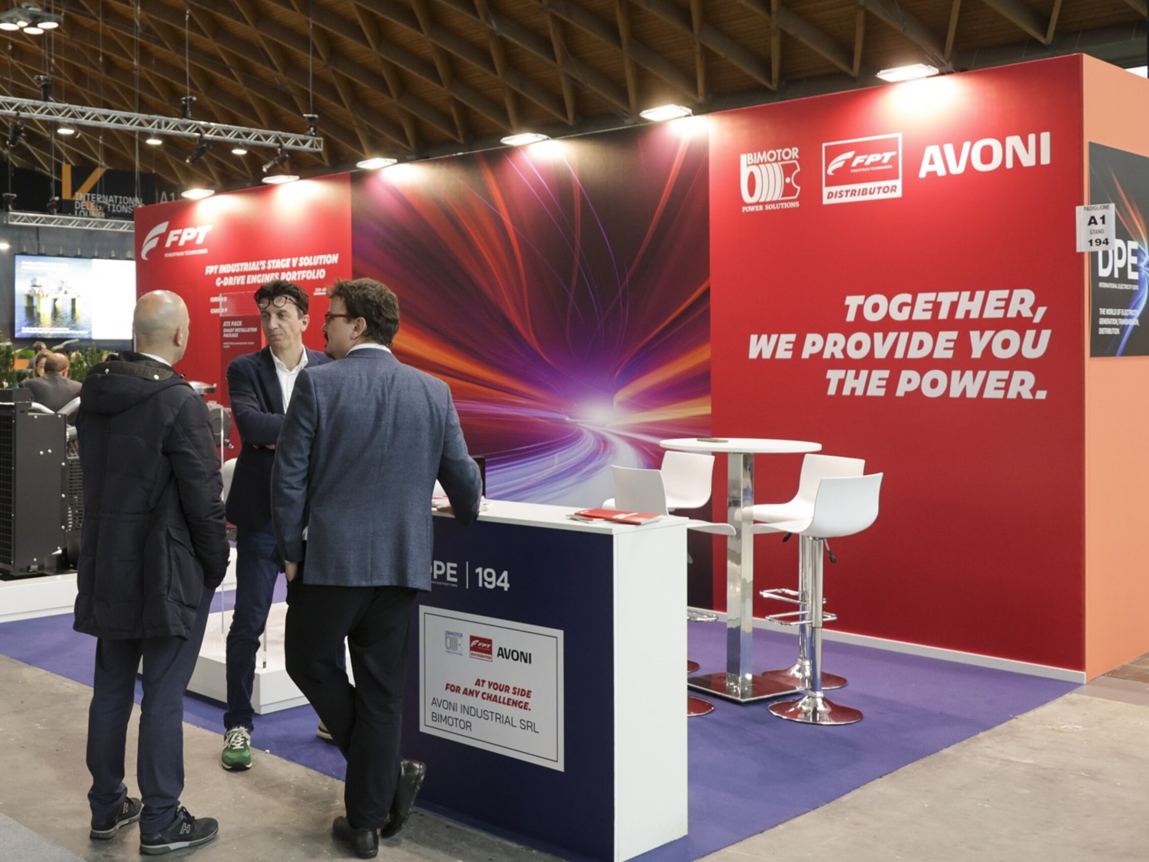 tre persone conversano durante DPE – International Electricity Expo, davanti a uno stand con un’ampia grafica a parete con la scritta 'Together, we provide you the power'