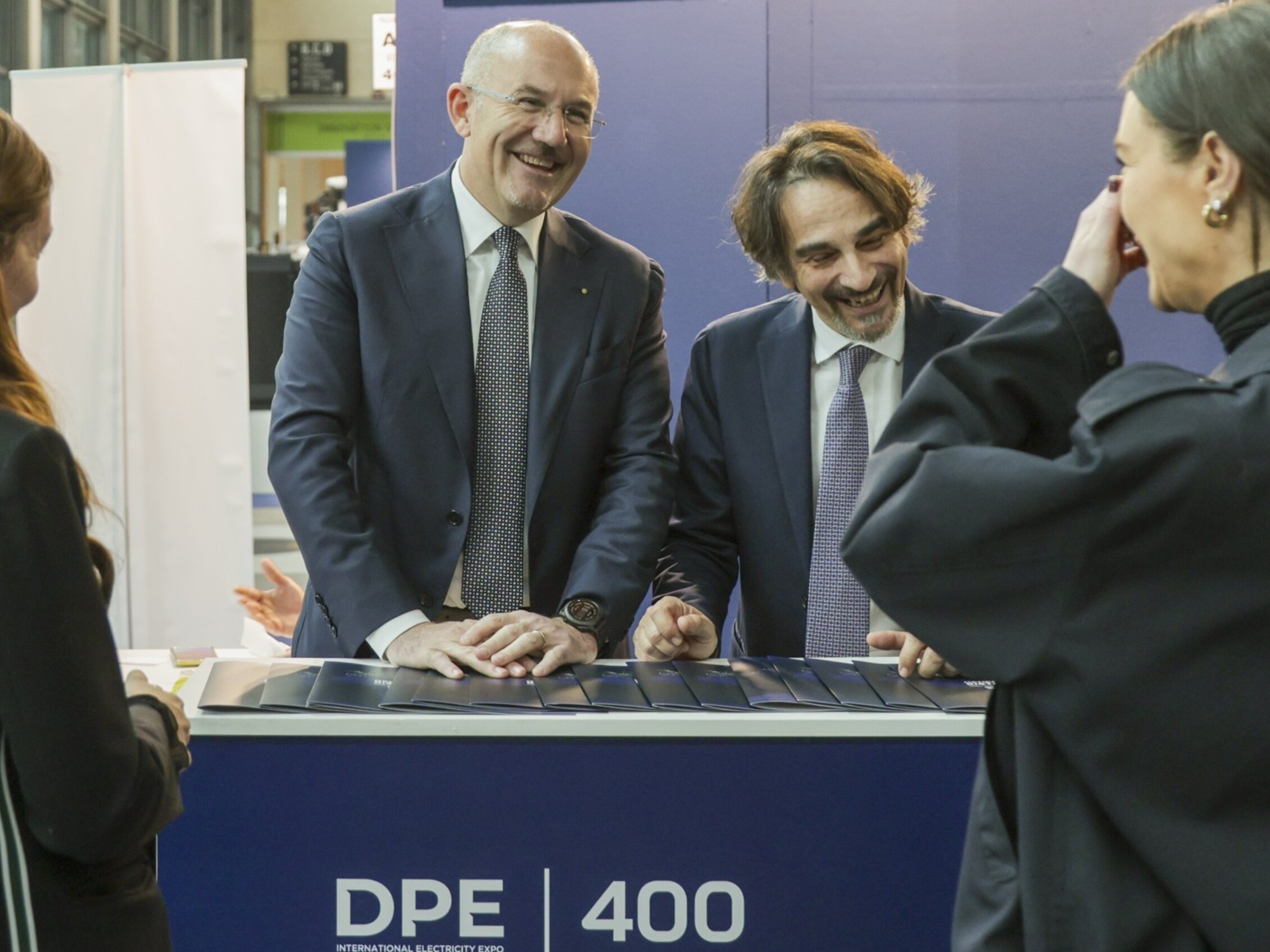 due espositori ridono insieme a due visitatori all'interno di uno stand di DPE distributed power europe