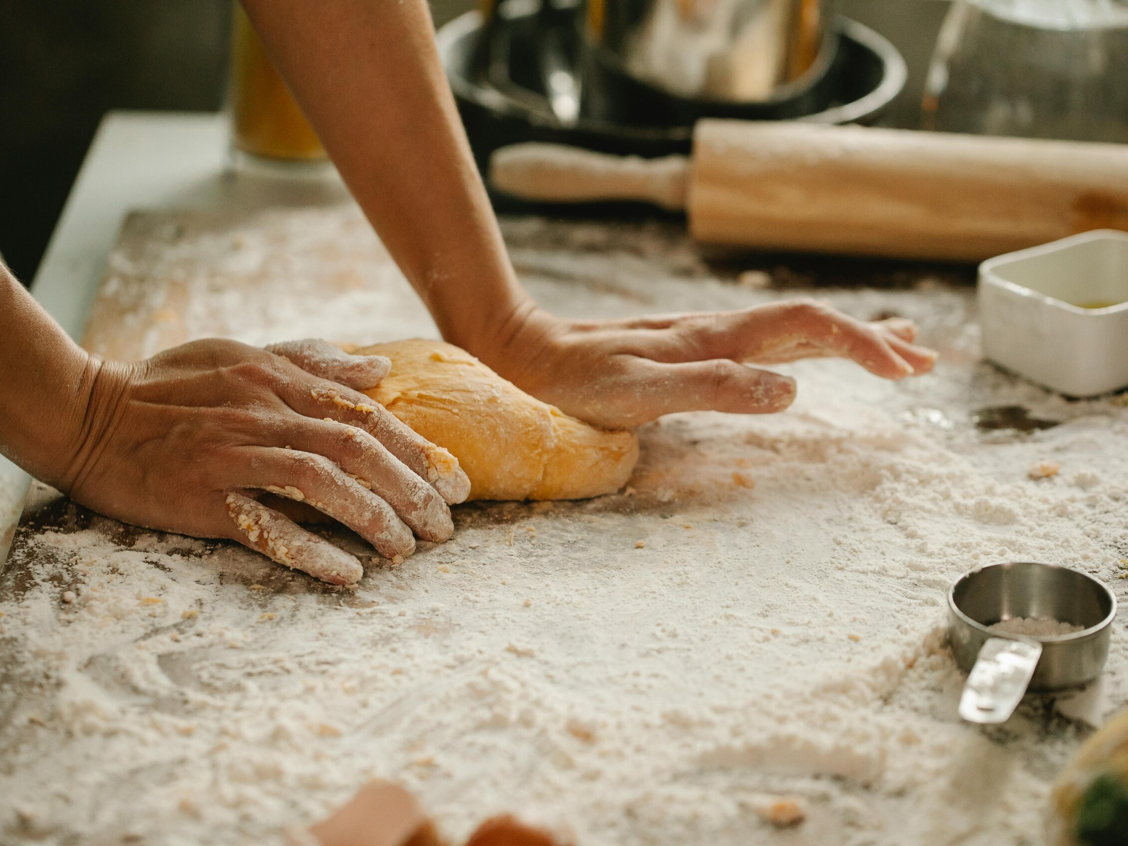 mani infarinate che lavorano un impasto su un piano da cucina